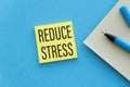 Paper notes with the words Reduce Stress on Yellow Sticky on blue table, top view. Royalty Free Stock Photo