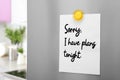 Paper with phrase Sorry, I Have Plans Tonight attached to refrigerator door with magnet in kitchen Royalty Free Stock Photo