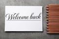 Paper with phrase Welcome Back and pencils on grey table, flat lay