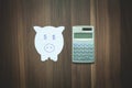 Paper piggy bank and calculator on the wooden background