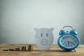 Paper piggy bank, stack of coins and alarm clock on wooden table. Time to invest your savings