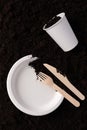 Paper plate and glass, wooden fork and knife on soil close-up, top view. Compostable or biodegradable dinnerware concept Royalty Free Stock Photo