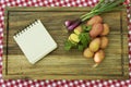 Paper for recipe on wooden board with potatoes, onion and parsnip leaves