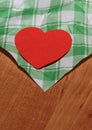 A paper red heart lies on a wooden surface on a white-green checkered surface