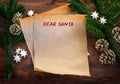 Paper sheet with text Dear Santa, between fir branches, cinnamon stars and pine cones on rustic dark wood, Christmas wish list or Royalty Free Stock Photo