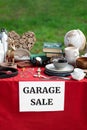 Paper with sign Garage sale and many different items on red tablecloth in yard Royalty Free Stock Photo