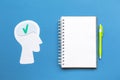 A paper silhouette of a thinking human head. Notebook with pen on a blue background. Mock up. Flat lay. Concept of