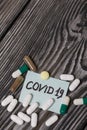 Paper sticker with the inscription COVID-19. Nearby are several pills of various shapes and colors. Lying on brushed pine boards Royalty Free Stock Photo