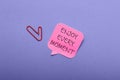 Paper with text Enjoy Every Moment on violet background Royalty Free Stock Photo