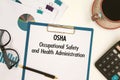 Paper with text OSHA - Occupational Safety and Health Administration on the table, calculator and cup of coffee