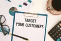 Paper with text TARGET YOUR CUSTOMERS on the table, calculator and cup of coffee