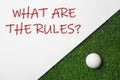 Paper with text WHAT ARE THE RULES and golf ball on grass