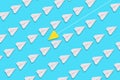 A paper yellow airplane is flying against the general direction of the white airplanes. Blue background. Flat lay. The concept of