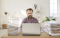 Portrait of serious and focused manager working on laptop among piles of documents. Royalty Free Stock Photo