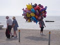 a balloon seller walks past two tourists walking alone the promenade in Paphos cyprus
