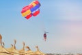 Parachute with two women in tandem over straw umbrellas on the beach