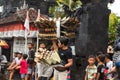 Parade on the street of the island of Bali. People gather scenery for the parade. A guy stands on the street holding a part of the