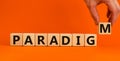 Paradigm word. Concept word `paradigm` on wooden cubes on a beautiful orange background. Male hand. Business and paradigm concep