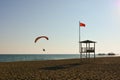 A paraglider flies over the evening sea beach. There is a sea rescue tower on the beach