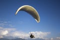 A paraglider flies on a white parachute against a blue sky with clouds and mountains