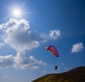 Paraglider flying above mount slope on suny cloudy sky background