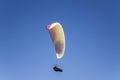 Paraglider in a gondola flies on a white parachute against a clean blue sky