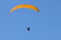 Paraglider pilot with an orange yellow glider is flying in the clear blue sky, recreational and competitive adventure sport, large