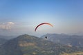 Paraglider on a red parachute flies over a green mountain valley under a clear blue sky aerial view Royalty Free Stock Photo