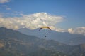 Paraglider on a red-yellow parachute flies against a background of green mountains and white clouds in the blue sky, aerial view Royalty Free Stock Photo