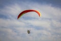 Paraglider on a red with yellow stripes paraglider flies in a blue sky with white clouds