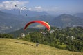 Paraglider takes off on a red parachute from the hillside against the background of a green mountain valley