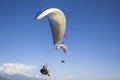 A paraglider on a white parachute in a clear blue sky against the backdrop of mountains and clouds and other pilots Royalty Free Stock Photo