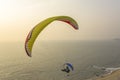 Paraglider on a yellow parachute and in a helmet flies over the beach and the ocean against the gray evening sky Royalty Free Stock Photo