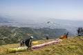 Paragliders on the hillside prepare to take off against the backdrop of the city in a green mountain