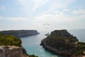 Paragliding over a paradisiac beach in between cliffs covered in pine trees, blue sky