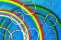 Parallel rows of small circles and large rainbow rings overlap rainbow and green arcs against a blue background.