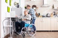 Paralysed elderly man in wheelchair typing on laptop working from home kitchen Royalty Free Stock Photo