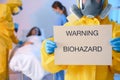 Paramedic holding sign with words WARNING BIOHAZARD in quarantine ward. Virus awareness