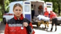 Paramedic posing for camera, ambulance crew transporting patient on background