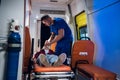 A paramedic puts on an oxygen mask on an unconscious woman lying on stretcher in the ambulance car