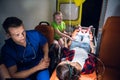 A paramedic and a sad little girl sitting beside a young woman lying on a stretcher in an ambulance