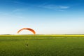Paramotor flying a rapeseed field with blue sky