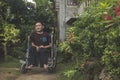 A paraplegic middle aged man in his wheelchair outside of his residence. An asian PWD living in a remote rural village