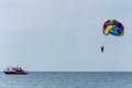 Parasailing in blue sky on a calm ocean with a red motorboat towing a persons suspended below a parachute by a harness. Flying on
