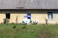 Parasol with small plastic table and two outdoor chairs in front of elongated dilapidated family house surrounded with uncut grass Royalty Free Stock Photo