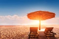 Parasol and sun bed loungers on empty tropical beach at sunset with beautiful warm colors, summer vacation holiday destination Royalty Free Stock Photo