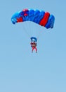 A paratrooper in a red suit descends under the canopy of a parachute