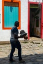 PARATY, RIO DE JANEIRO, BRAZIL - DECEMBER 28, 2019: A local man carries a pile of hats in front of colorful colonial buildings in