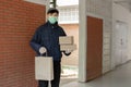 Parcel delivery concept the standing-tall post carrier who is wearing pale grey cap carrying one bag on left hand and two boxes on