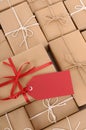 Red gift tag with background of brown paper packages in a row, copy space, vertical Royalty Free Stock Photo